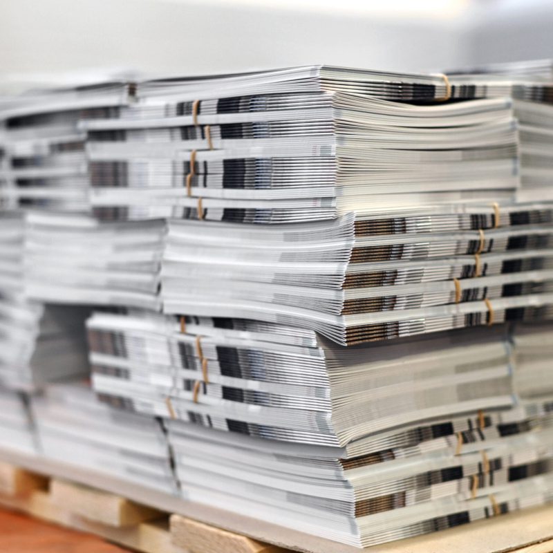 Stack of freshly printed catalogs Soft focus of sheets of freshly printed catalogs stacked together on wooden pallet in typography workshop