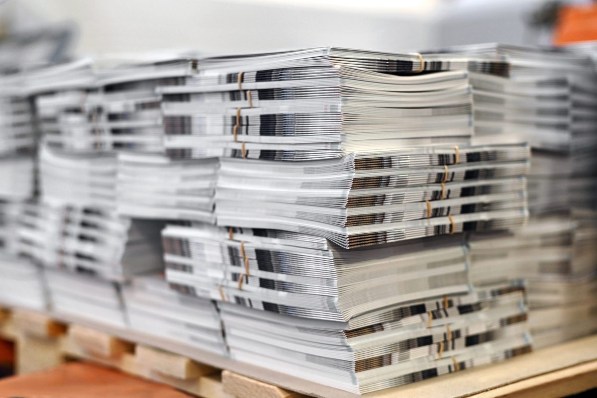 Soft focus of sheets of freshly printed catalogs stacked together on wooden pallet in typography workshop